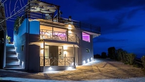 A modern two-story building with a balcony and outdoor lighting. - Relax in Style at Ben’s Homes Panorama (Nopigia)