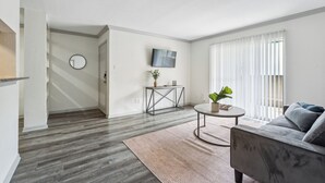 Ein modernes Wohnzimmer mit einem grauen Sofa, einem runden Couchtisch und einem an der Wand befestigten Fernseher.