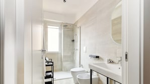 A modern bathroom with a glass shower, a toilet, a bidet, and a sink with a mirror. - 1-Bed apartment with balcony near subway (Milan)