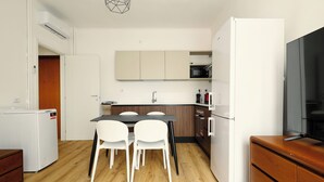 A compact kitchen with a dining table, chairs, a refrigerator, a microwave, and a television. - 1-Bed apartment with balcony near subway (Milan)