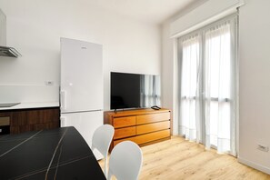 Een moderne keuken met een koelkast, een houten kast met een flatscreen televisie en een eethoek met een zwarte tafel en witte stoelen.