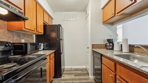 Une cuisine de taille réduite, avec des meubles de rangement en bois, un réfrigérateur noir, une cuisinière et un évier.