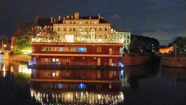 A large, multi-story building with a restaurant on the ground floor, located by a body of water.
