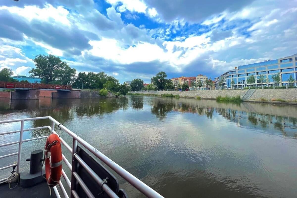 Vista de un río desde un bote, con un flotador en la cubierta, un puente y edificios al fondo.