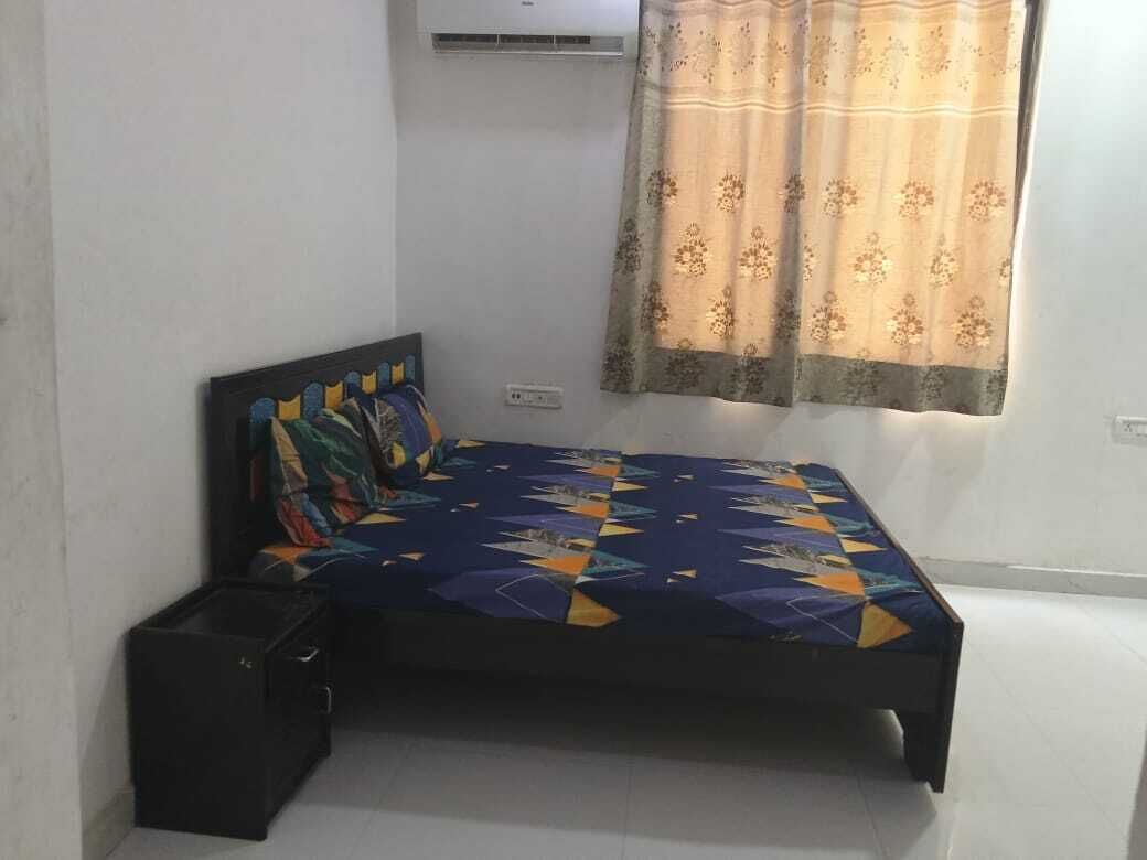A bedroom with a bed, a nightstand, a black storage box, and a window with curtains.