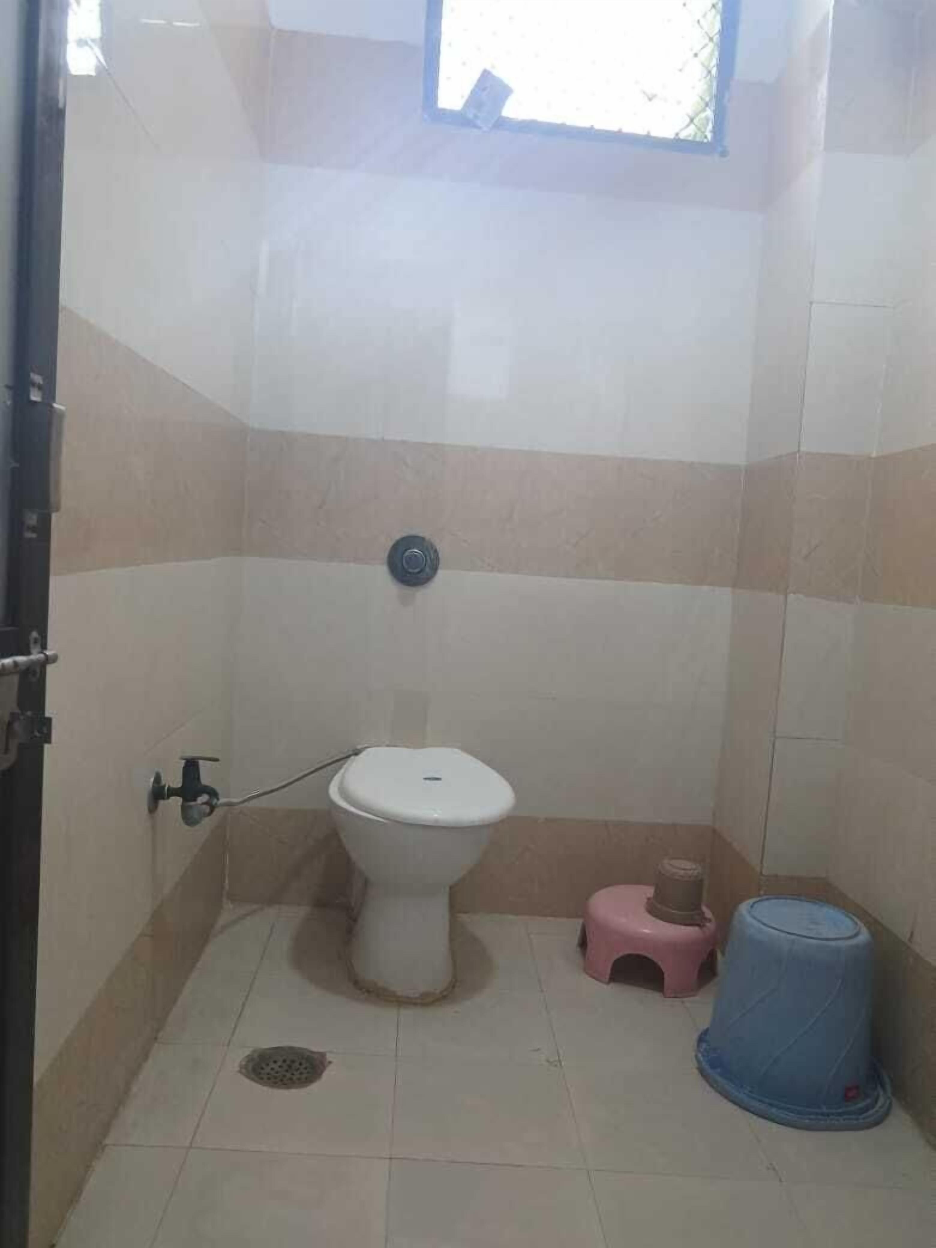 A small bathroom with a toilet, a pink stool, and a blue trash bin.