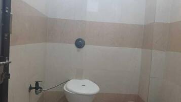 A small bathroom with a toilet, a pink stool, and a blue trash bin.
