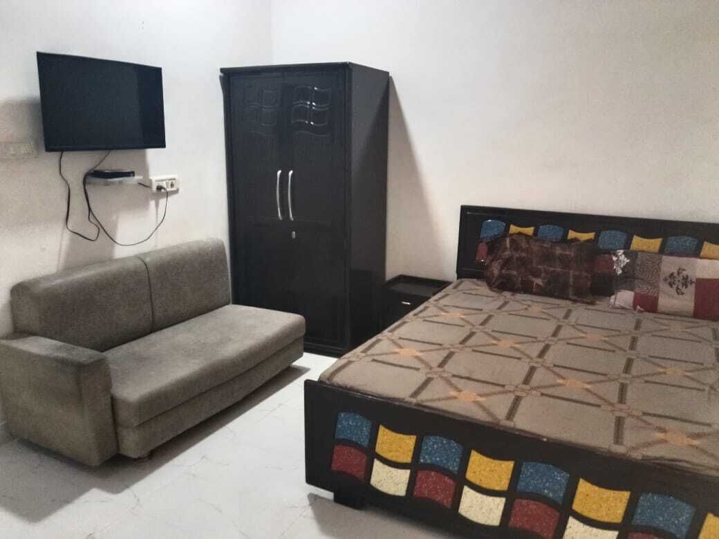 A bedroom with a bed, a sofa, a wardrobe, and a TV mounted on the wall.