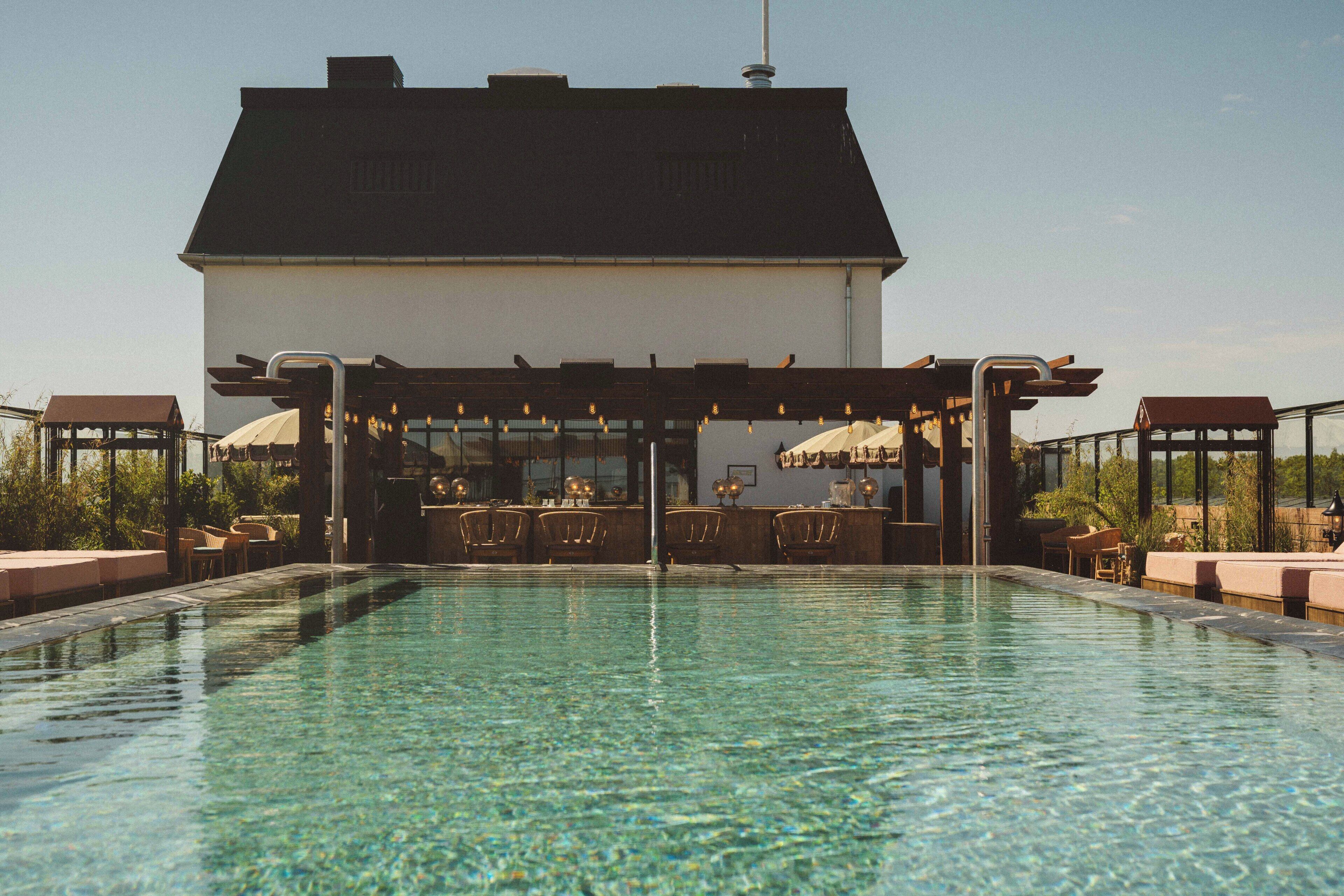 Zona de piscina con bar y asientos, rodeada por un edificio de techo oscuro.