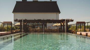 Zona de piscina con bar y asientos, rodeada por un edificio de techo oscuro.