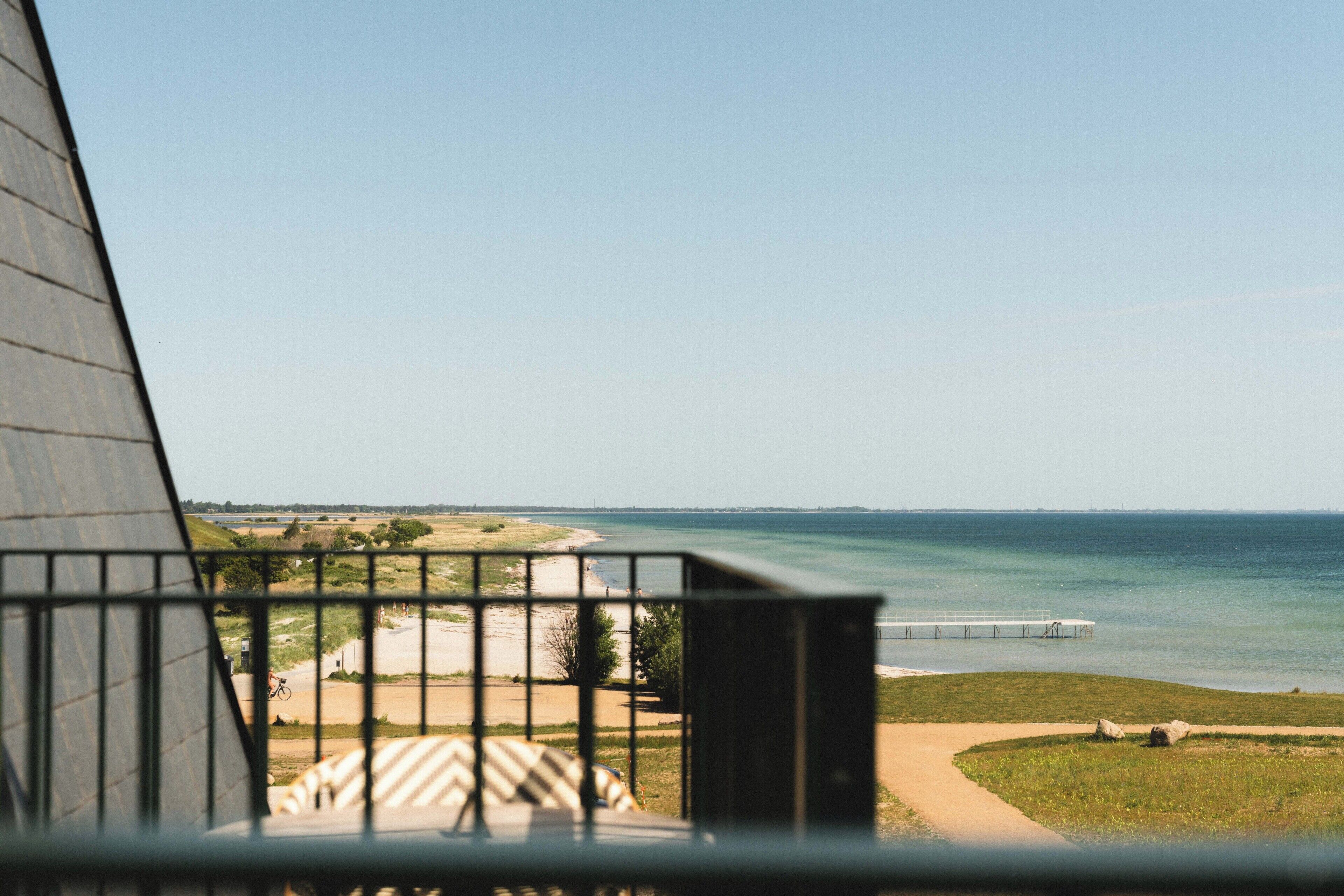 A view through a window with a metal railing, a sandy beach, a grassy area, and a body of water.