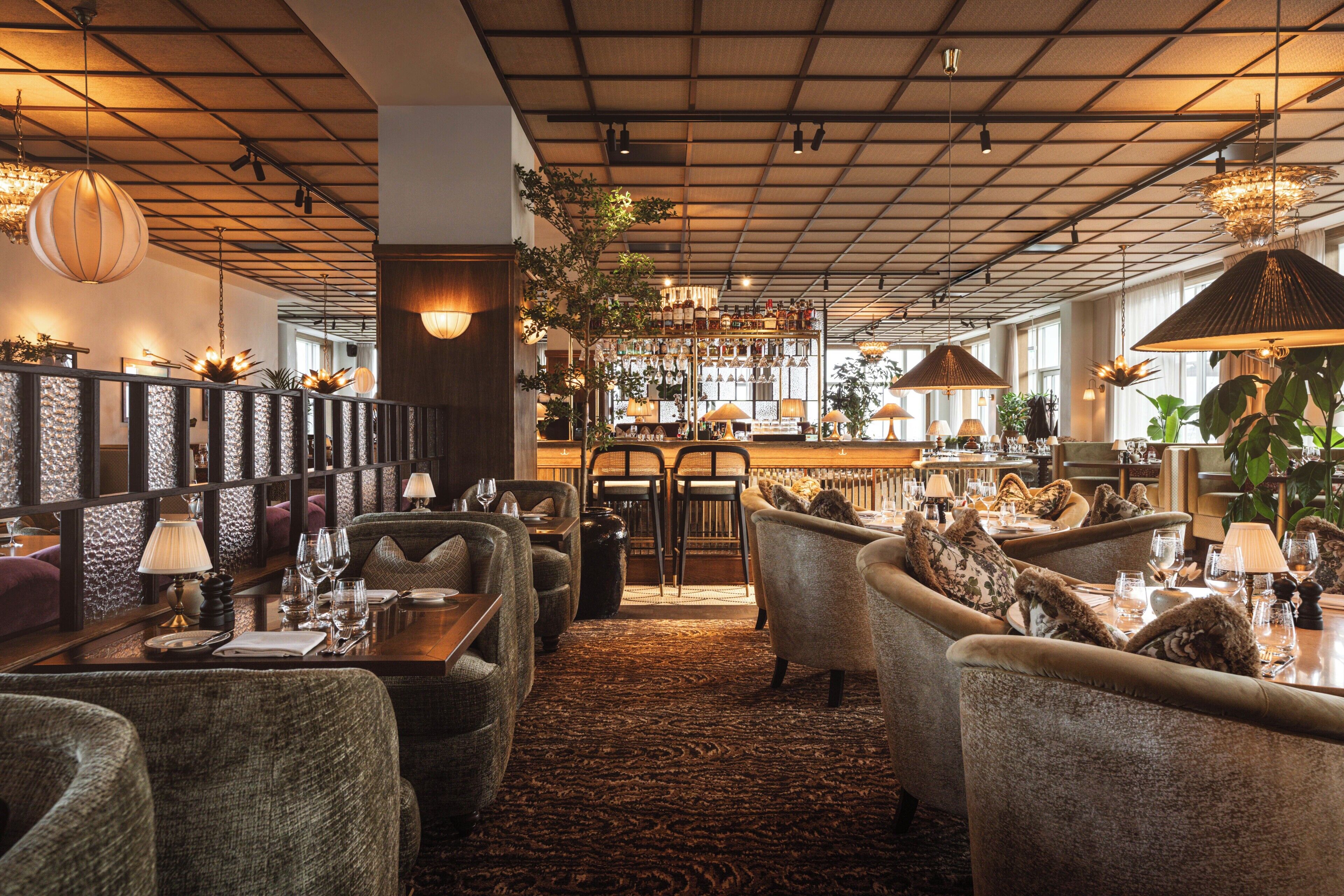 A restaurant with high ceilings, hanging lamps, and a bar area.