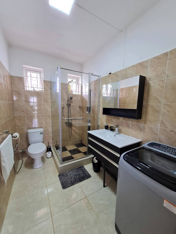 Un baño con inodoro, cabina de ducha, lavabo y lavadora Samsung.
