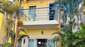 Ein zweistöckiges Gebäude mit Balkon, geschlossenem Eingangstor und umgebender Bepflanzung.
