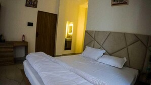 A bedroom with a large bed, a wooden dresser, a ceiling fan, and a door leading to another room. - Hotel Riyansh  (Ukhimath)