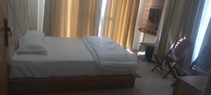 A neatly made bed with a wooden headboard, a wooden nightstand, and a chair with a cushioned seat. - Hotel Riyansh  (Ukhimath)