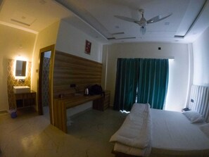 A hotel room with a bed, a wooden bench, a small table, a mirror, and a ceiling fan. - Hotel Riyansh  (Ukhimath)