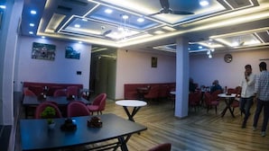 A modern restaurant interior with a wooden floor, red upholstered booths, and a contemporary ceiling design with recessed lighting. - Hotel Riyansh  (Ukhimath)