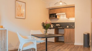 A compact kitchen with wooden cabinets, a microwave, a coffee machine, and a small dining area with two white chairs and a table.