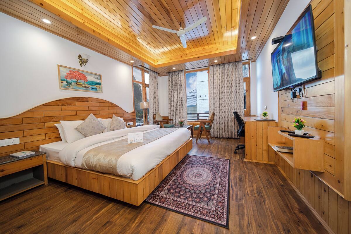 Quarto com painéis de madeira, cama, escrivaninha, televisão e janela com cortinas.