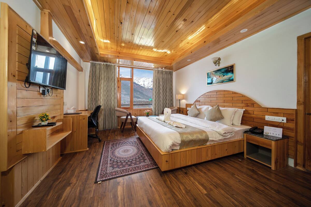Quarto com painéis de madeira, cama, escrivaninha, cadeira e televisão.