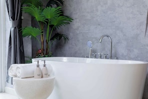 Un baño moderno con una bañera independiente, un lavabo grande y una planta.