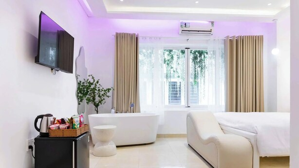 A modern hotel room with a flat-screen TV, a bathtub, a sofa, and a small refrigerator. - Ari Boutique Hotel (Ho Chi Minh City)