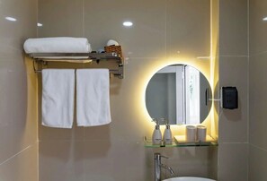 Un baño moderno con un estante de vidrio que contiene artículos de aseo, un espejo redondo con luz y dos toallas colgadas en un perchero.