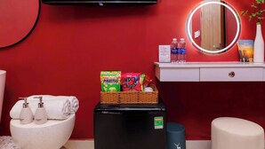 A bathroom with a red wall, a black refrigerator, a white sink, a mirror, and toiletries. - Ari Boutique Hotel (Ho Chi Minh City)
