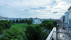 A view of a residential area with a large building in the background, a grassy field, and a balcony with a railing. - Ari Boutique Hotel (Ho Chi Minh City)