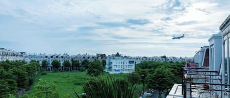 Une vue d’un quartier résidentiel, avec un grand immeuble en arrière-plan, un champ d’herbe et un balcon doté d’une balustrade.