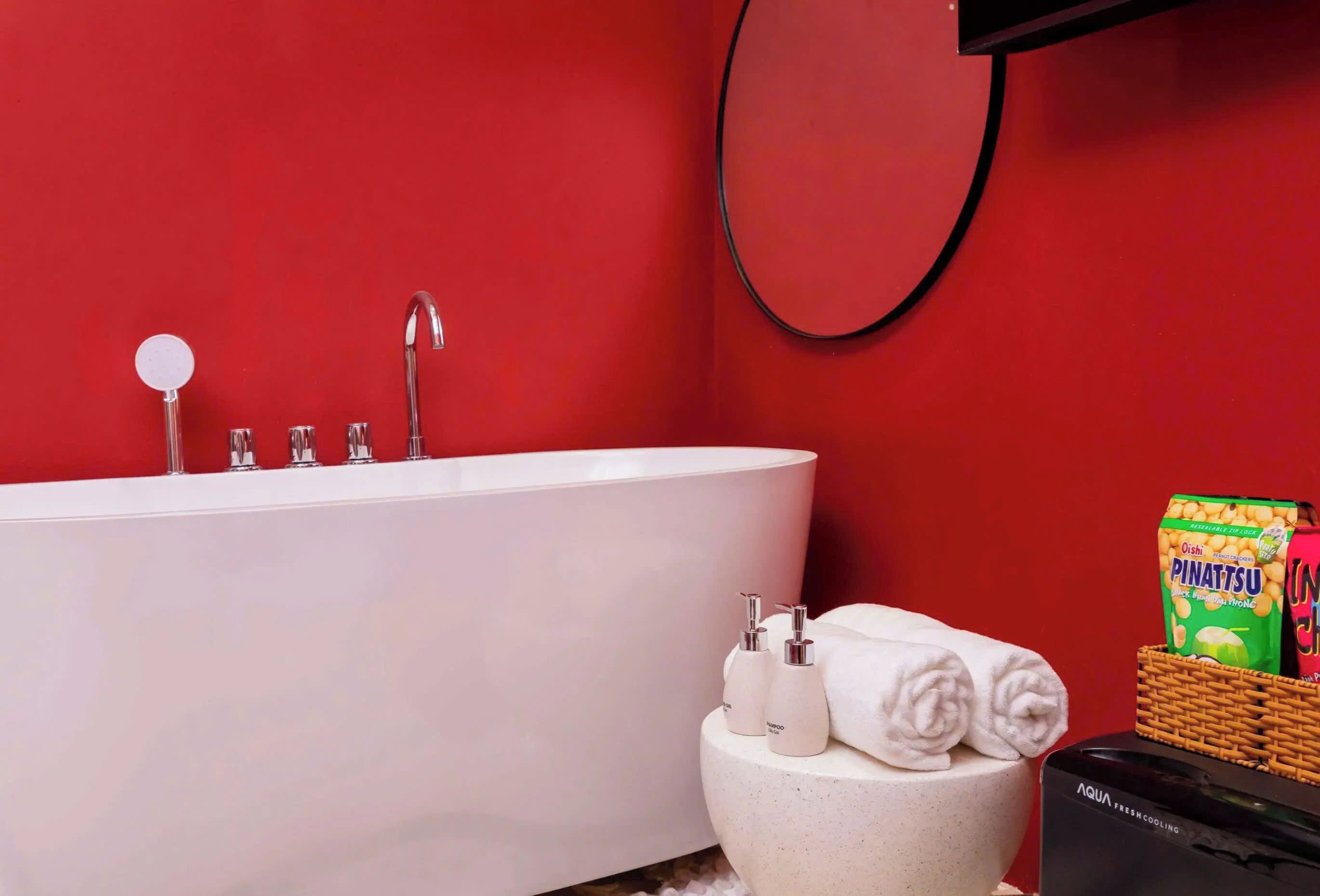 A modern bathroom with a white bathtub, a round mirror, and a small sink with two bottles.