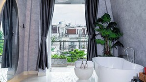 A modern bathroom with a large bathtub, a white sink, and a view of a cityscape through large windows. - Ari Boutique Hotel (Ho Chi Minh City)