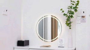 A bathroom vanity with a round mirror, a black tissue box, a white vase with a plant, and a sign on the wall. - Ari Boutique Hotel (Ho Chi Minh City)
