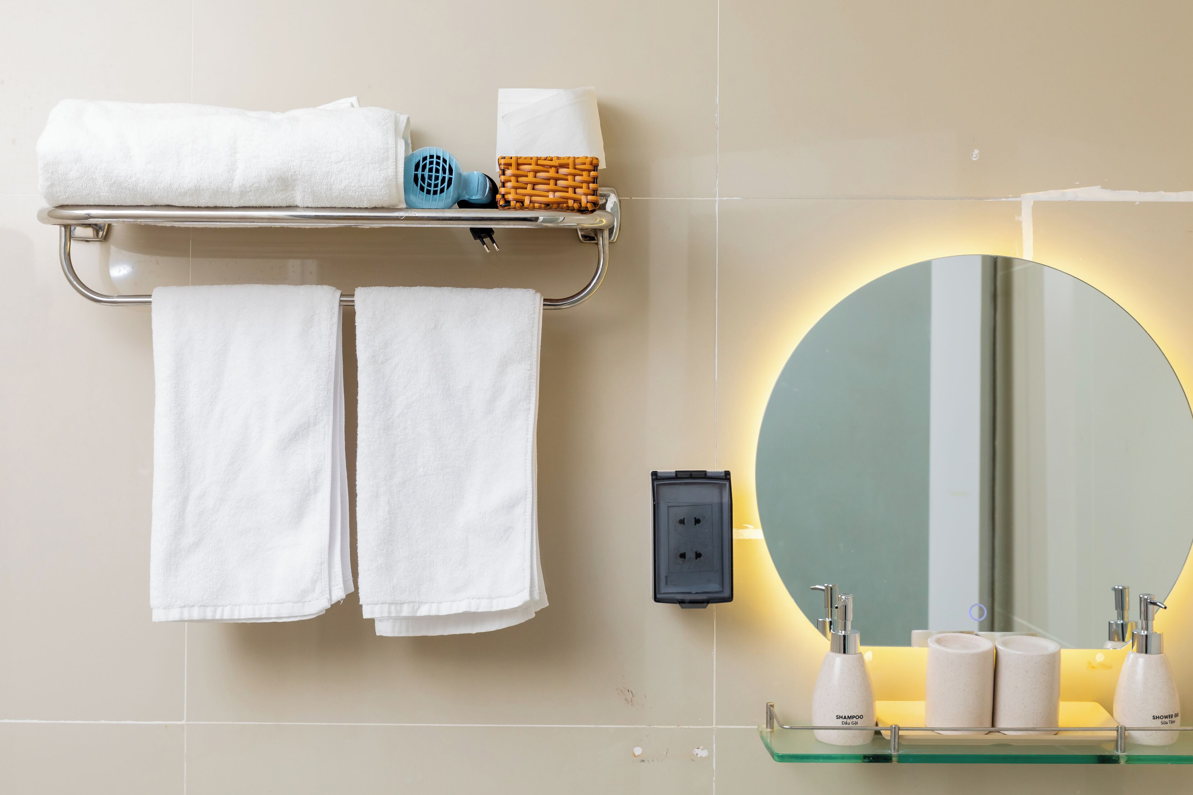 A bathroom with a round mirror, two towels, a shelf with toiletries, and a wall socket.