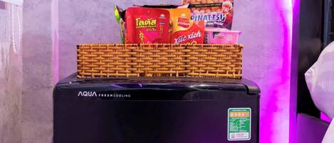 A black refrigerator with a wicker basket on top containing snacks and a pink cup.