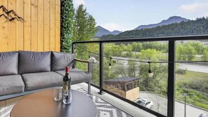 A modern room with a sofa, a round table, and a view of mountains and greenery. - Apres Ski | DT | MtnView | TopFloor | AC | Sleep 6 (Golden)