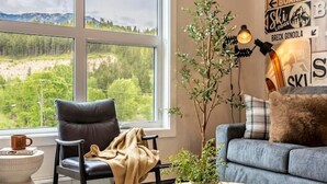 A living room with a large window, a black leather chair, a grey sofa, a wooden coffee table, and a poster on the wall. - Apres Ski | DT | MtnView | TopFloor | AC | Sleep 6 (Golden)