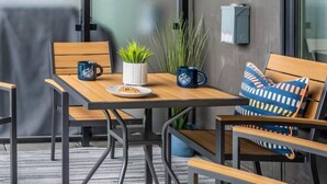 A modern outdoor seating area with wooden tables and chairs, a potted plant, and a wall-mounted electrical box.