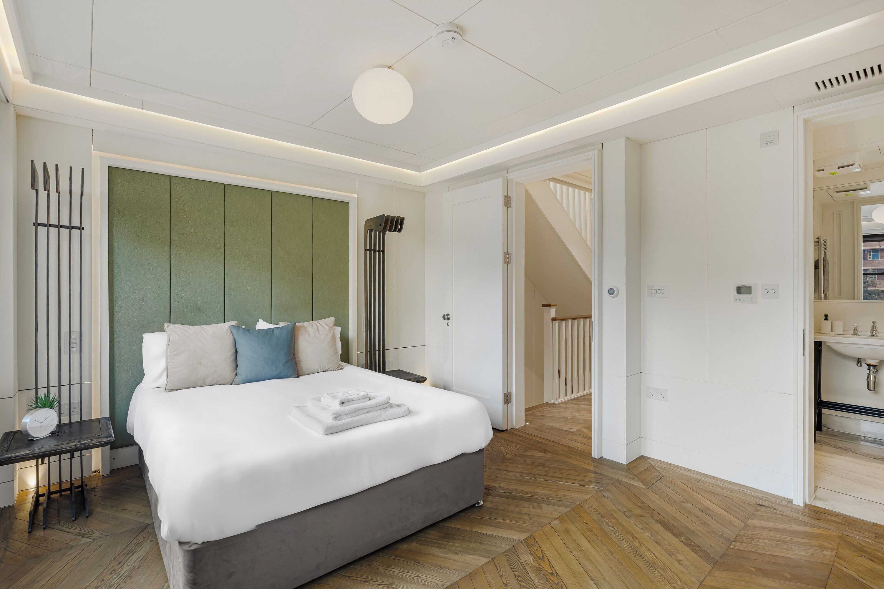 Un dormitorio moderno con una cama grande, una mesita de noche, una pared de acento verde y vistas al baño.