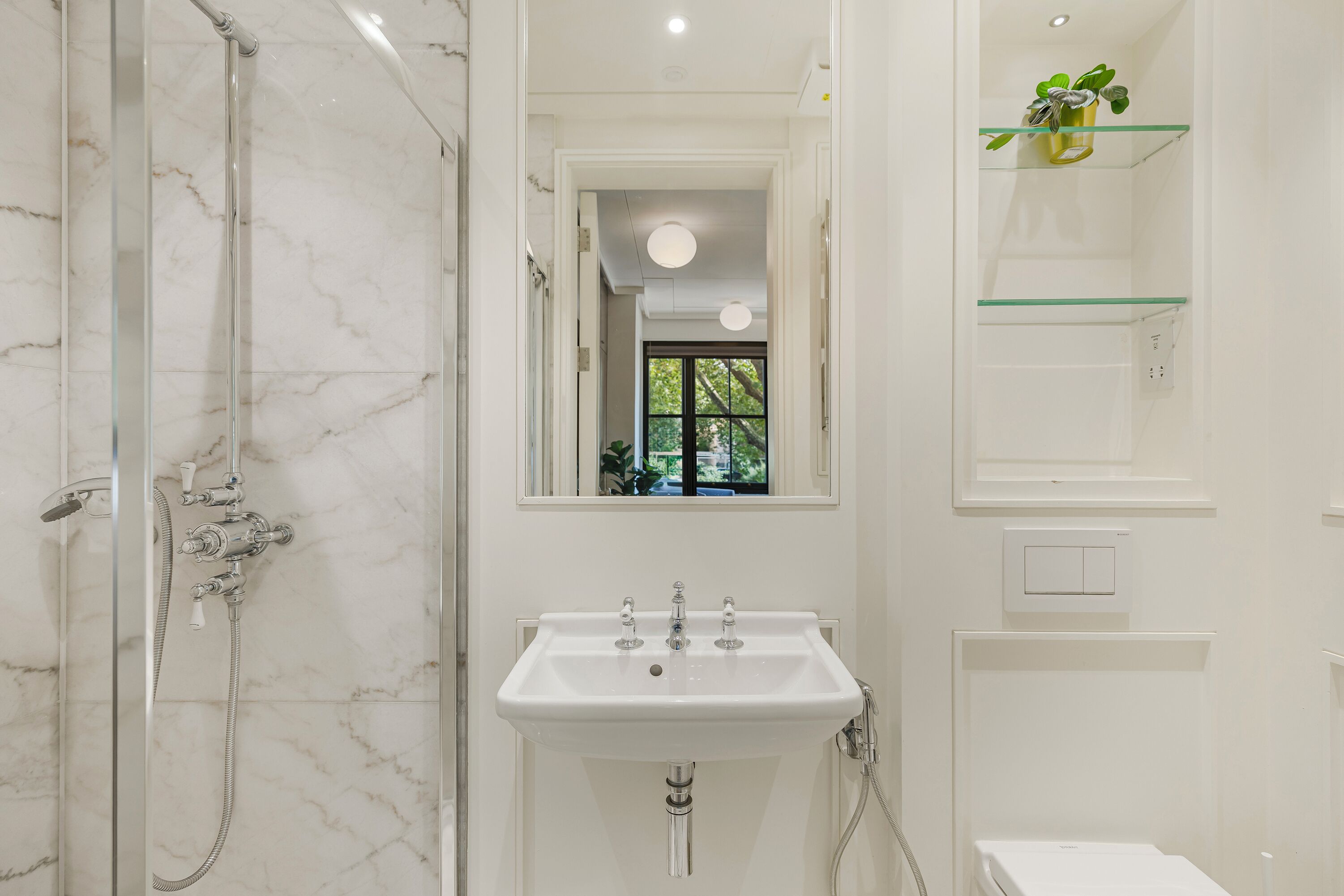 Un bagno con cabina doccia in vetro, lavandino bianco e specchio sopra.