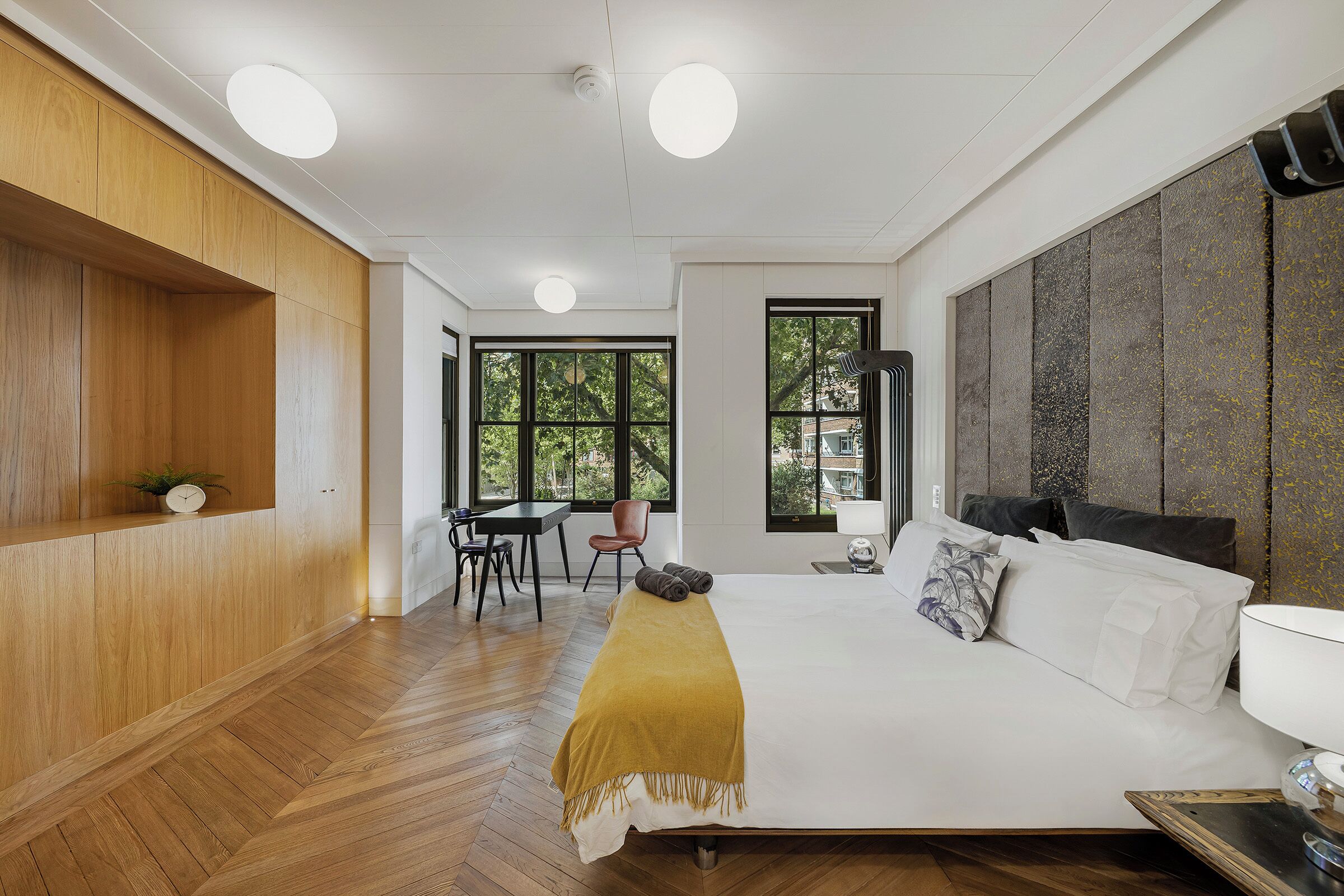 Ein modernes Schlafzimmer mit einem großen Bett, Holzböden, einem Schreibtisch und Blick ins Freie durch große Fenster.