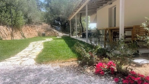A covered outdoor seating area with tables and chairs, a stone pathway, and a grassy lawn. - Agreen Country House Myrtle (Sardegna)
