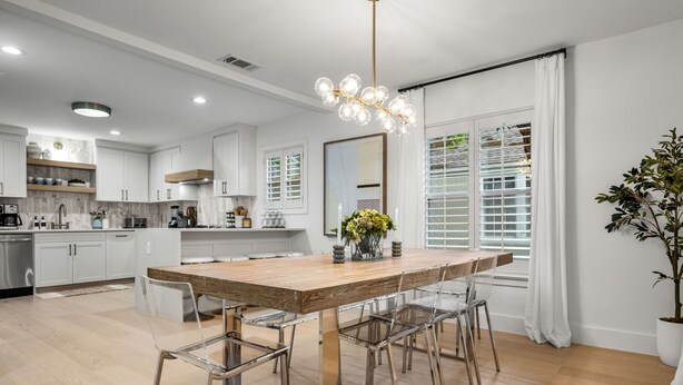 A modern kitchen with white cabinetry, a wooden dining table, and clear chairs. - The Lyndzee-Luxury Downtown Haven, Pool, Sleeps 16 (Dallas)