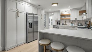 A modern kitchen with white cabinetry, stainless steel appliances, and a central island with stools. - The Lyndzee-Luxury Downtown Haven, Pool, Sleeps 16 (Dallas)