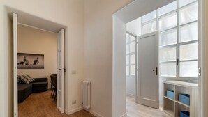 A spacious hallway with a wooden floor, a radiator, and a door leading to a room with a black sofa and a wall-mounted zebra painting. - CS Termini National Apt No. 3 (Rome)