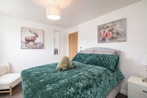 Un dormitorio con cama, una silla, una mesita de noche, una lámpara y dos cuadros colgados en la pared.