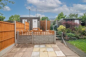 A fenced backyard with a brick building, a wooden gate, and a stone wall.