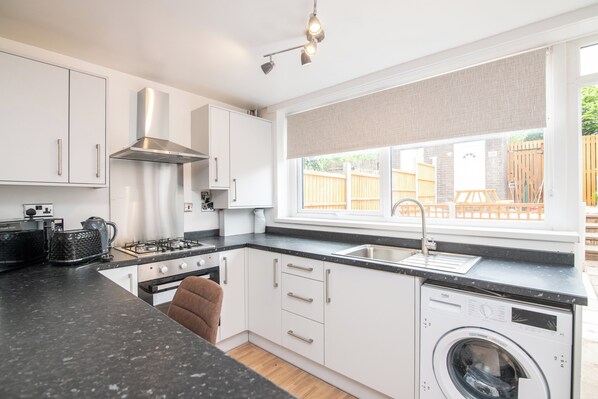 A modern kitchen with a built-in washing machine, a stove, and a window with a view of a backyard.