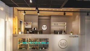 A B&B hotel reception area with a bar, shelves of bottled beverages, and a reception desk. - B&B Hotel Berlin Airport-Nord (Berlin)